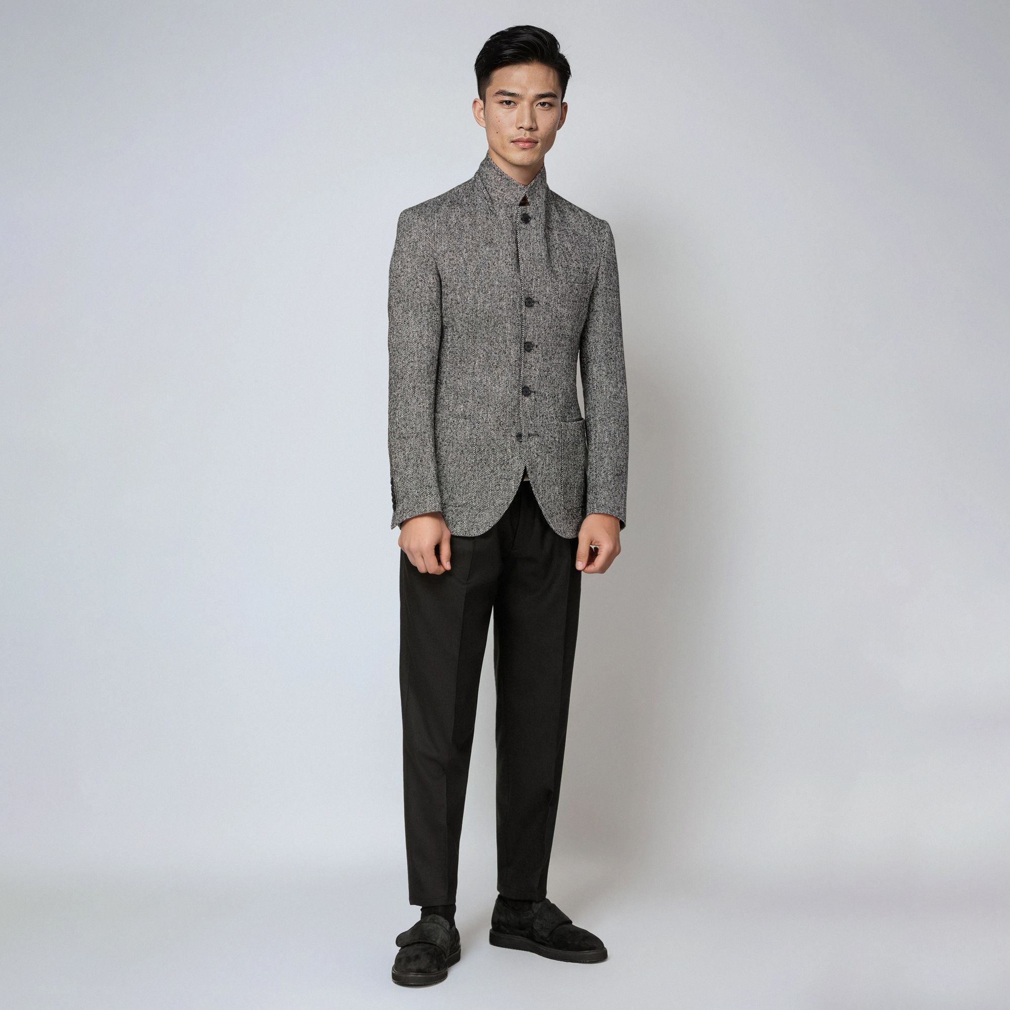 Uomo con total look Elio Evan: giacca bouclé grigia chiusa con colletto alto e pantaloni neri.