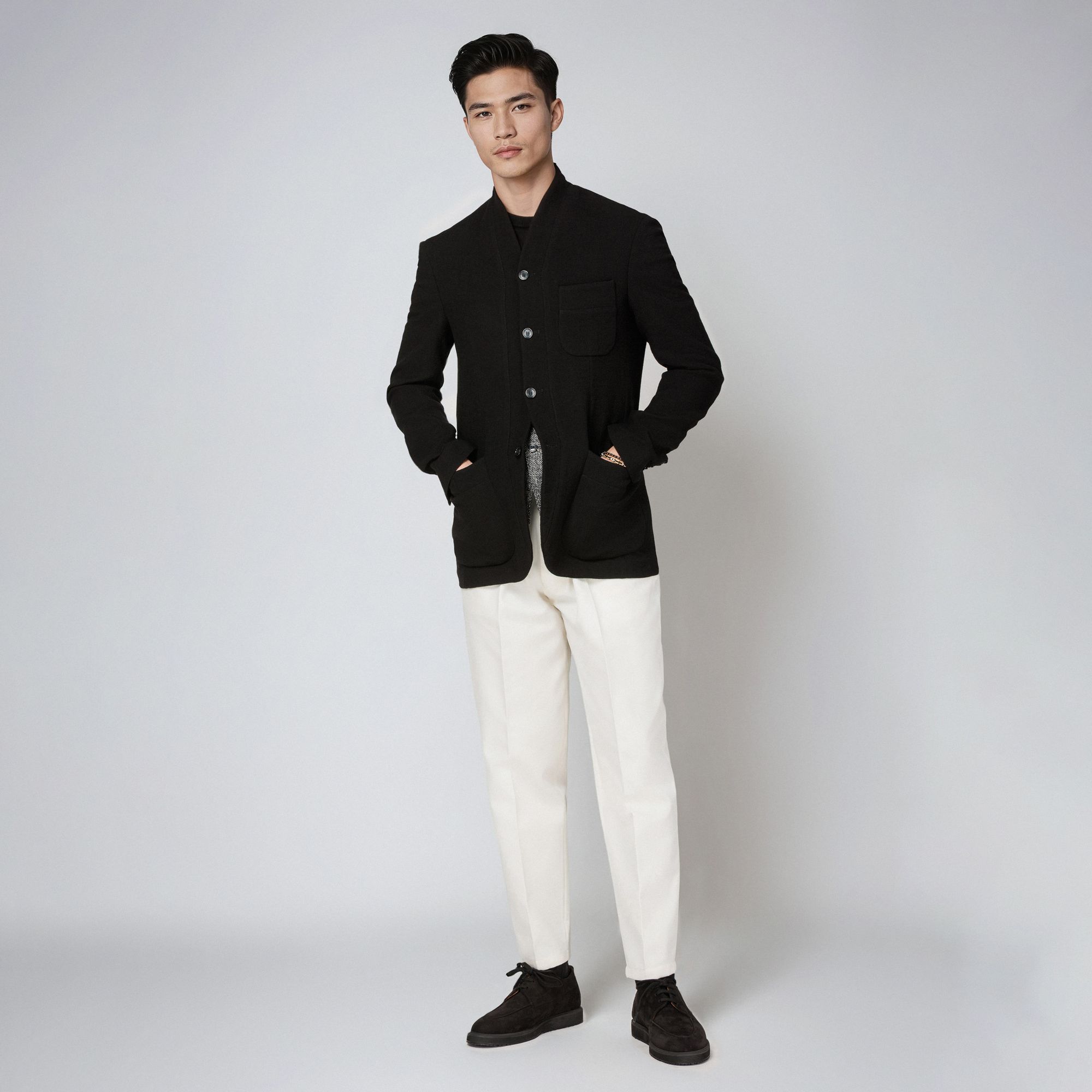Uomo con total look Elio Evan: giacca minimal nera in lana con collo shawl e pantaloni bianchi.